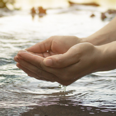 Hands cupping water over a stream