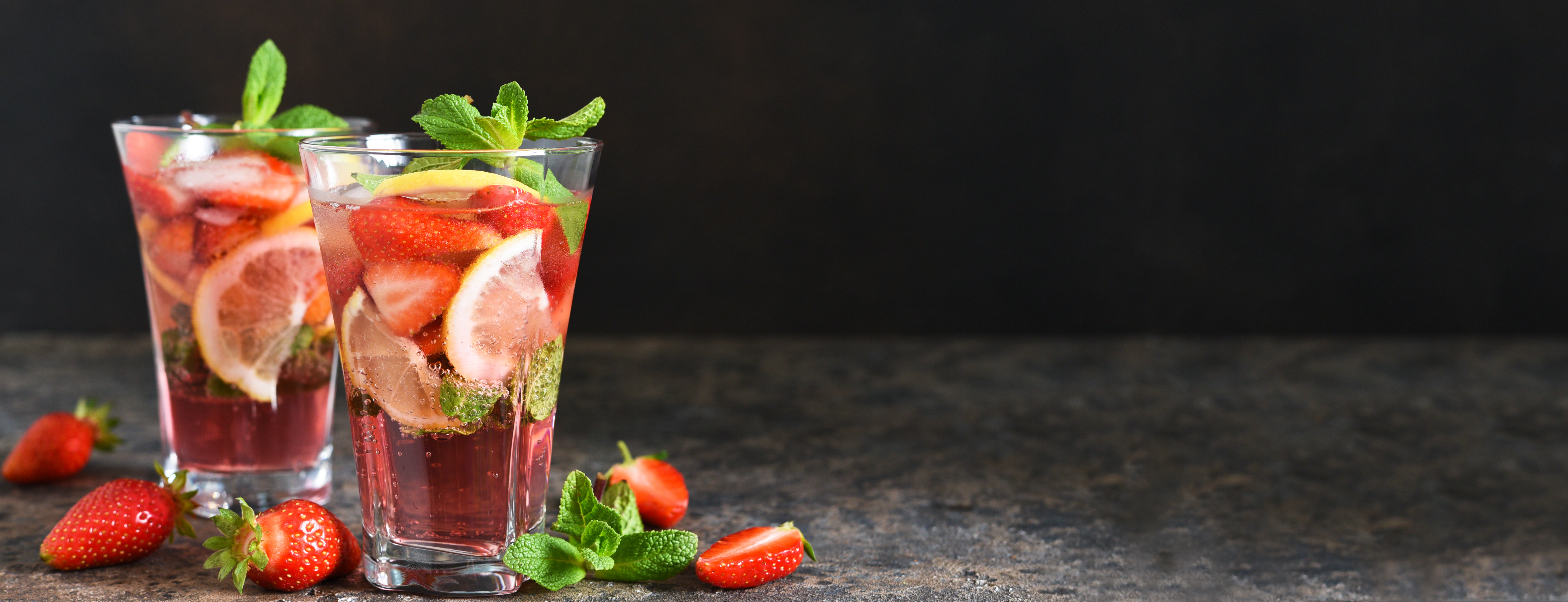 Lemonade with strawberries and mint on a dark concrete background. Summer cold drink.