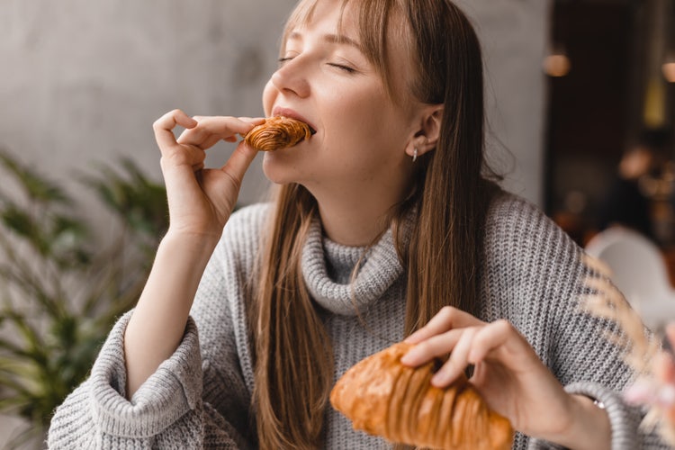 Persona consumiendo un croissant de hojaldre recién horneado, destacando su textura crujiente, capas laminadas y apariencia artesanal