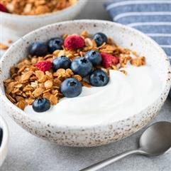 Tazón de yogur cremoso con granola, arándanos y frambuesas, presentado como una opción nutritiva para desayuno o snack