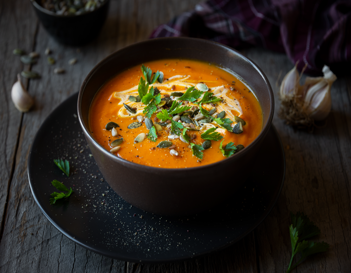 Creamy roasted pumpkin soup served in a dark bowl, garnished with fresh parsley, pumpkin seeds, and a swirl of cream on a rustic wooden table