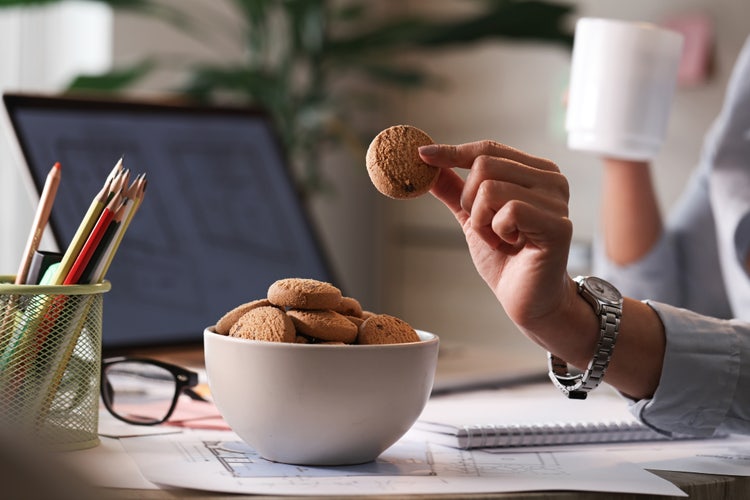 Persona tomando una galleta de un tazón en un espacio de trabajo, destacando una experiencia de snack durante la jornada laboral