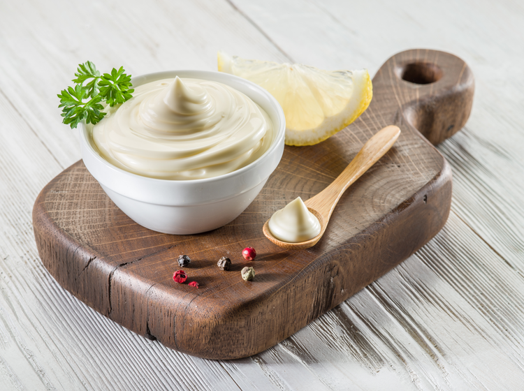 Creamy citrus dip in a white bowl garnished with parsley, placed on a wooden board with lemon wedge, peppercorns, and a wooden spoon, showcasing fresh ingredients and gourmet condiment presentation