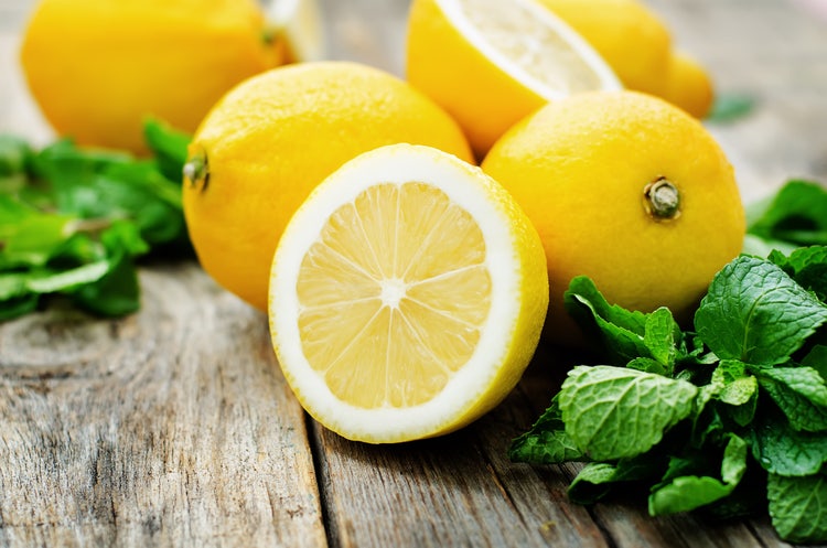 Sliced fresh lemon with juicy segments and green mint leaves on a rustic wooden table, highlighting vibrant citrus fruits and natural ingredients for healthy recipes and refreshing beverages