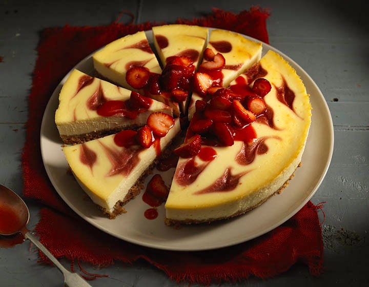 Yellow cheescake, topped with strawberries and cut into slices