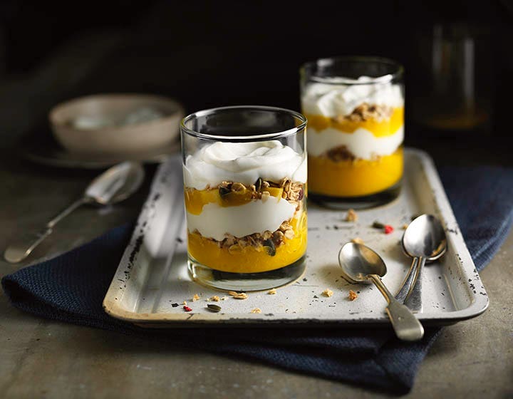 Two glasses of yoghurt with yellow fruit and granola