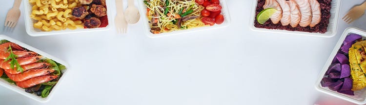 Meal trays with colorful dishes including shrimp, pasta, fish, and vegetables on a white background
