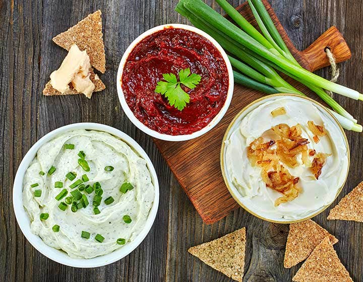 Tres tipos de dip gourmet servidos en tazones: crema con cebollín, salsa roja con cilantro y dip de cebolla caramelizada, acompañados de pan crujiente y cebollas verdes frescas, ideales para botanas y aperitivos caseros.