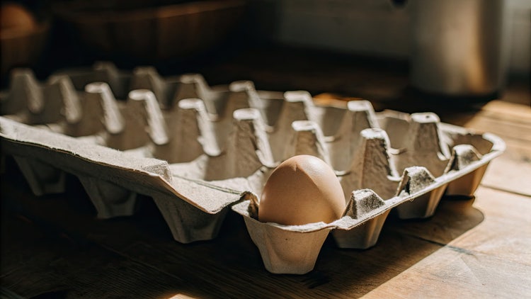 Huevo marrón colocado en charola de cartón para huevos sobre mesa de madera, concepto de producto fresco y empaque ecológico para cocina saludable.