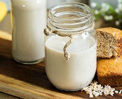 Vaso de leche vegetal servido en frasco de vidrio junto a pan integral y granos, bebida saludable ideal para dietas veganas y desayunos nutritivos.