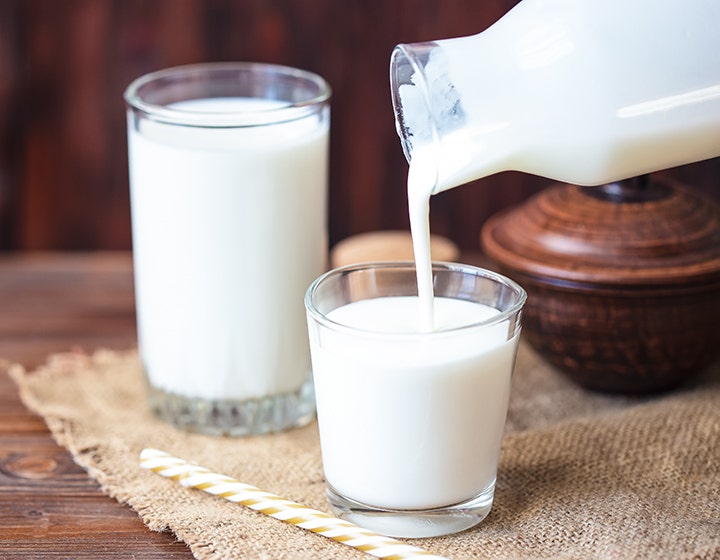 Milk being poured into a glass next to a full glass of milk
