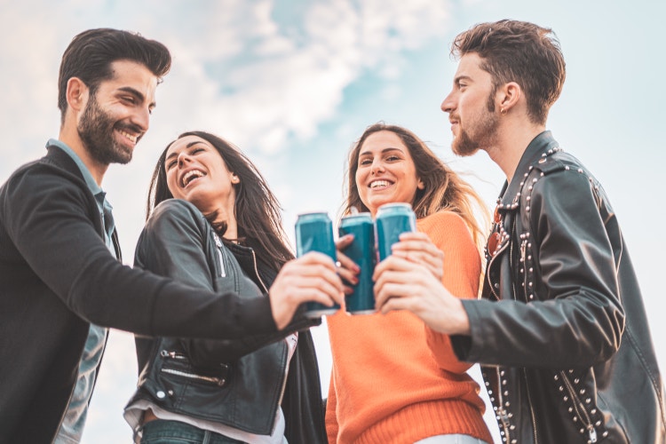 Two guys and two girls smiling and toasting with canned beers outdoor. Carefree youth having fun outdoors.